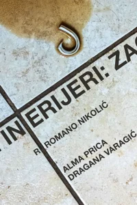 Plakat predstave Lijepi interijeri: Zagreb — naziv predstave i autorski podaci ispisani su dijagonalno na pločicama od hrapavog kamena, s metalnom kukom u gornjem dijelu slike