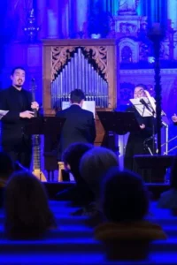 Ansambl Responsorium nastupa pred publikom u crkvenom prostoru osvijetljenom plavim svjetlom, uz orgulje i trombone.